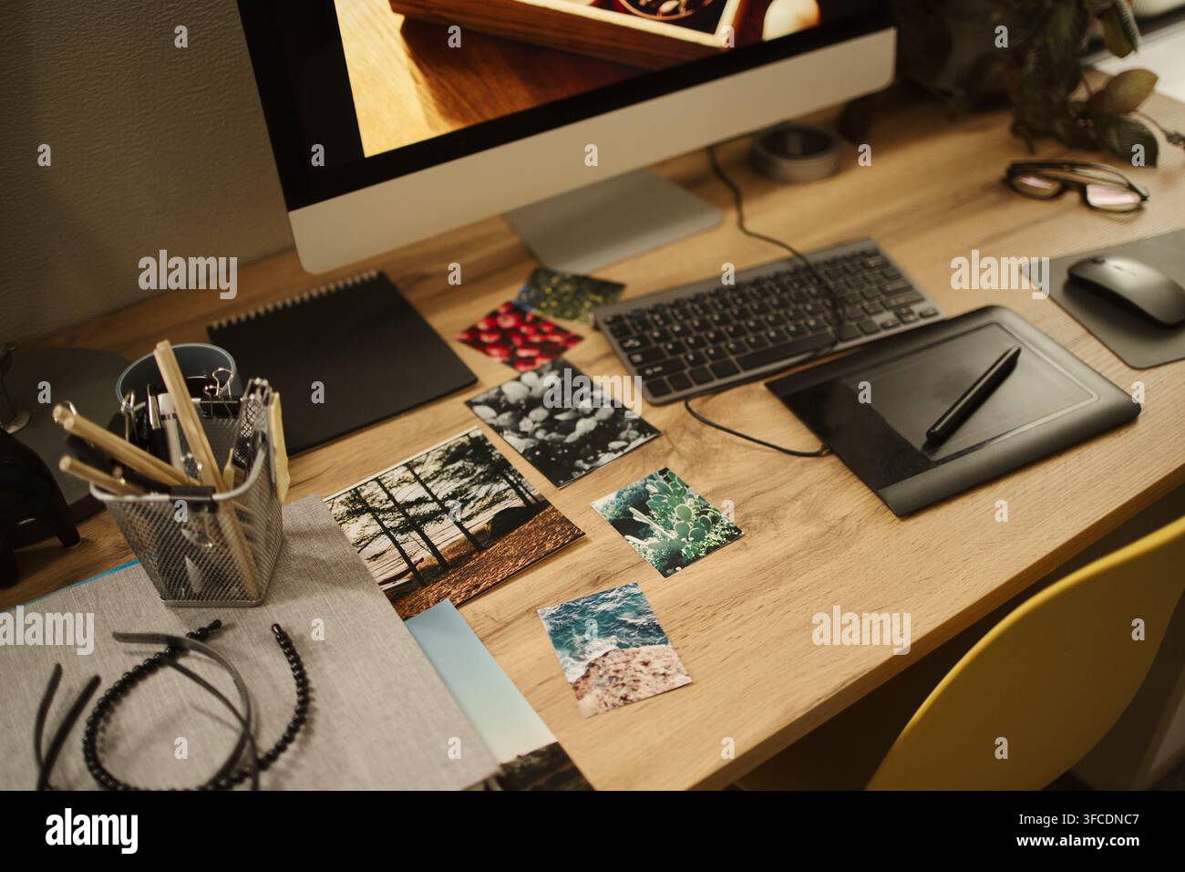 Espace de travail de graphiste comprenant un écran d'ordinateur, un clavier, une tablette graphique et des photos de référence imprimées sur un bureau en bois, représentant un flux de travail créatif, prise de vue à angle élevé Banque D'Images