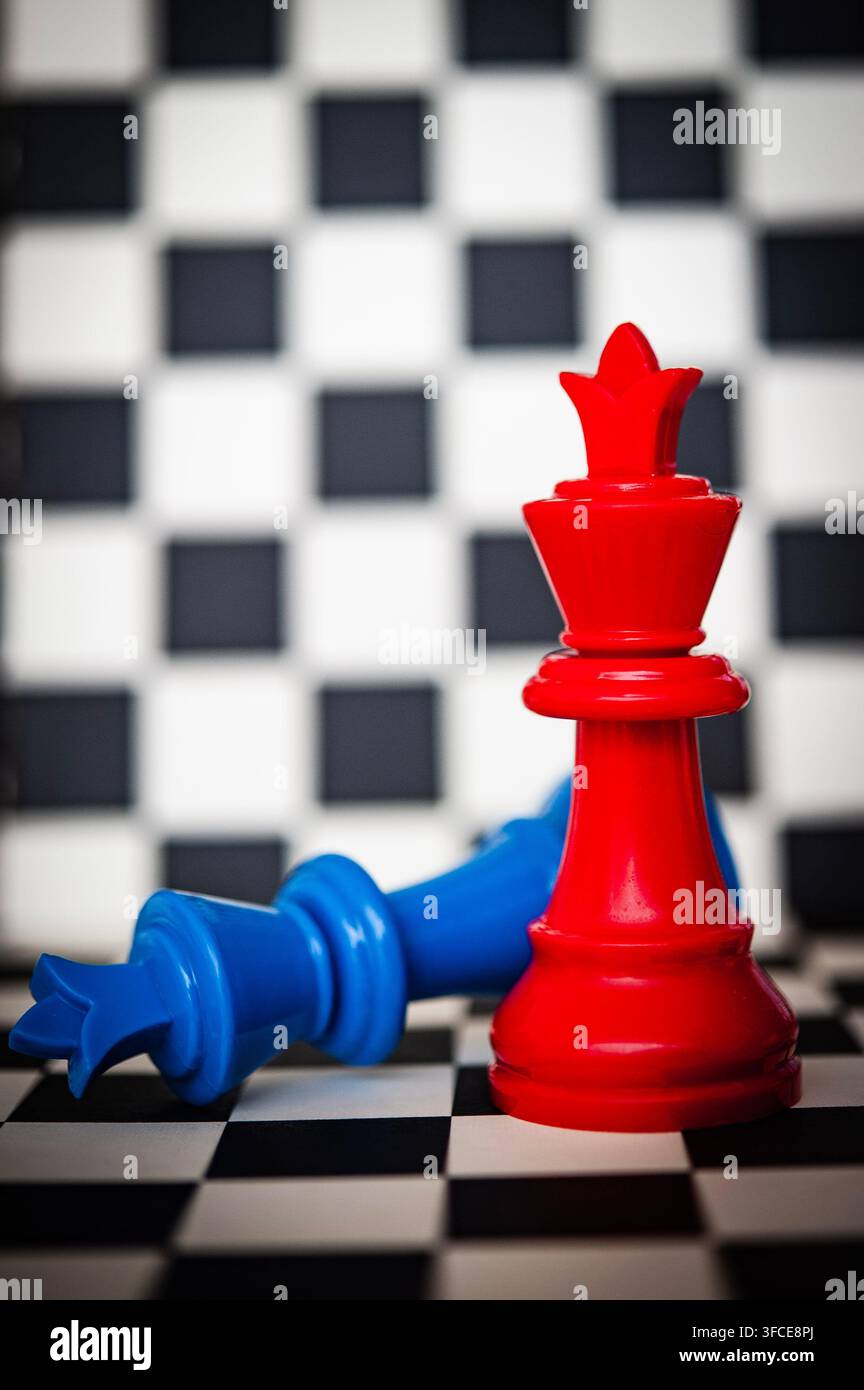 Roi d'échecs rouge debout tandis qu'un roi bleu gît vaincu sur un échiquier noir et blanc, symbolisant la victoire et la compétition Banque D'Images