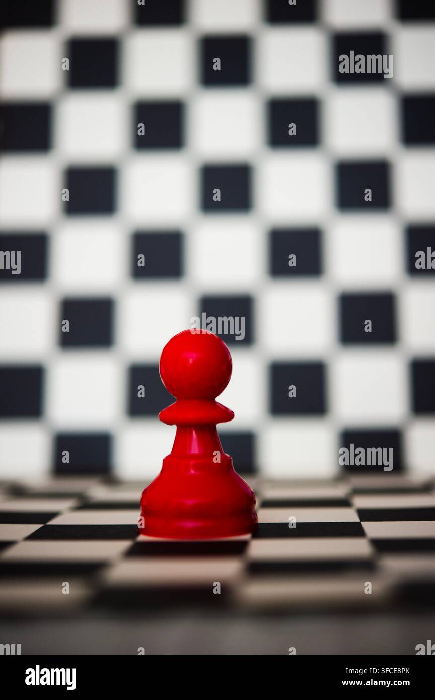 Pion d'échecs rouge unique sur un échiquier noir et blanc avec fond d'échiquier flou et espace de copie généreux au-dessus Banque D'Images