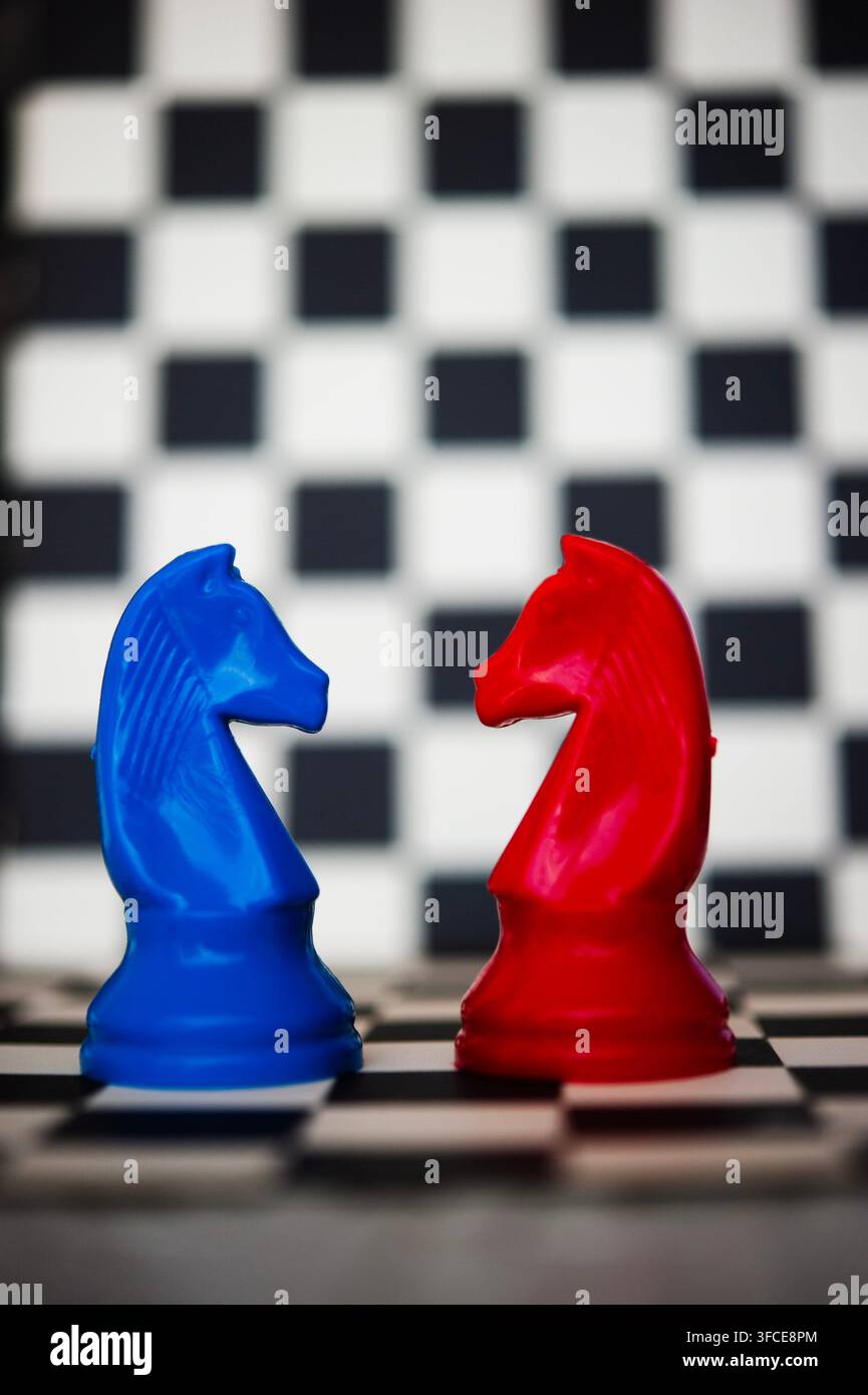 Chevaux d'échecs bleus et rouges se faisant face sur un échiquier noir et blanc, suggérant rivalité, stratégie et confrontation Banque D'Images