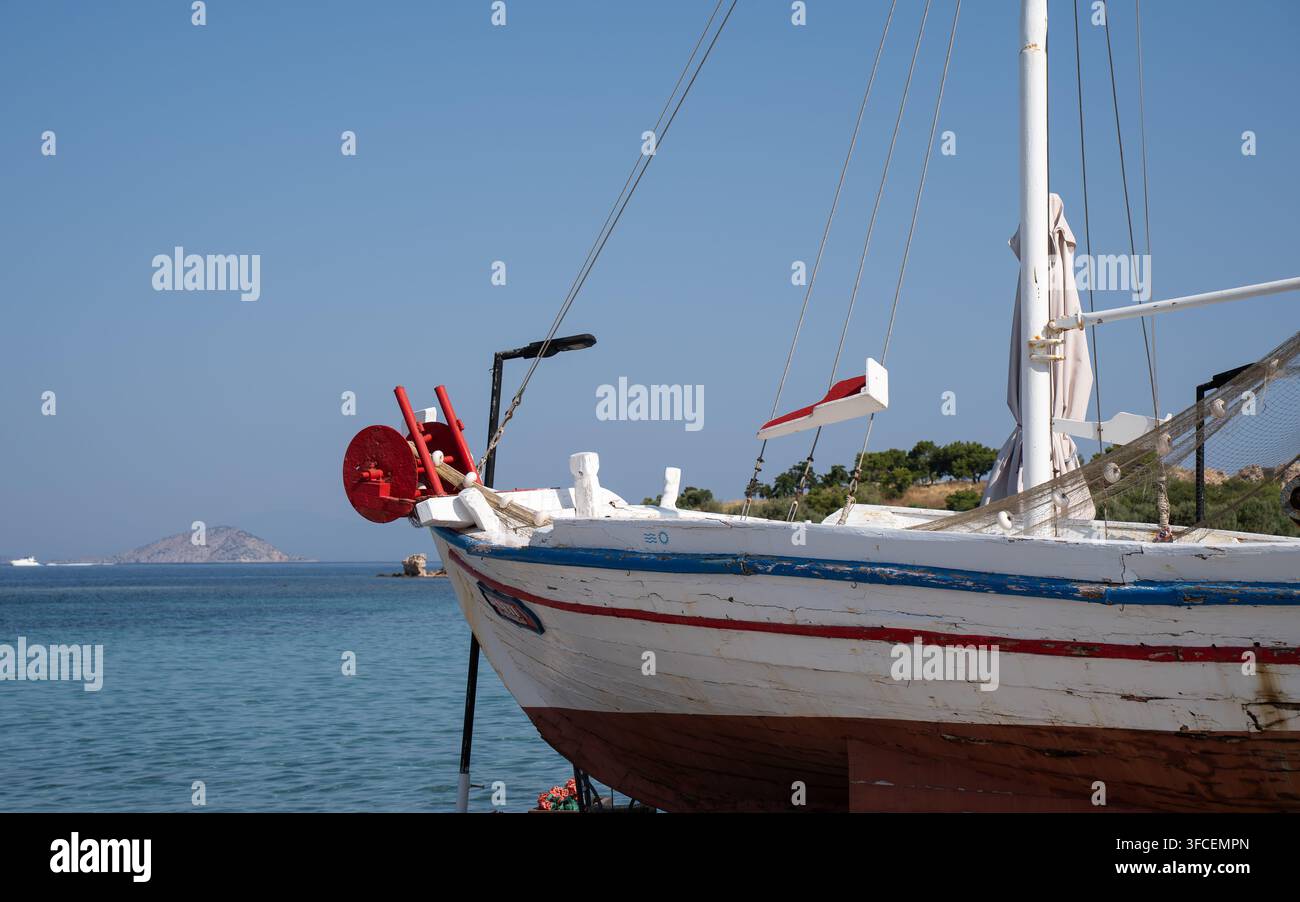 Petit bateau de pêche blanc et rouge flottant sur une eau bleue calme sous un ciel dégagé dans un paysage côtier paisible Banque D'Images