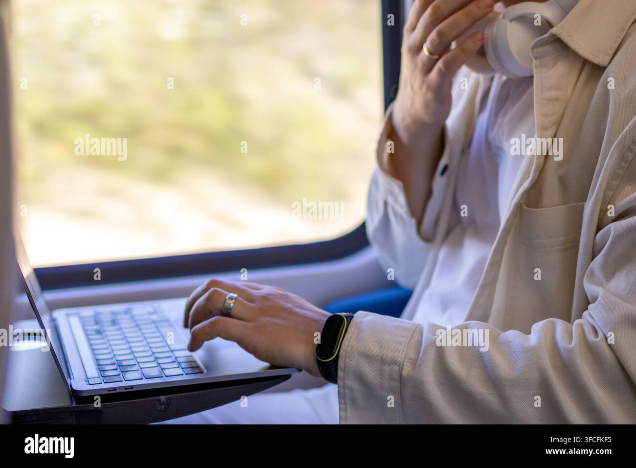 Voyageur d'affaires utilisant un ordinateur portable à côté d'une fenêtre de train avec des écouteurs autour du cou. Concept de travail mobile, voyages d'affaires, style de vie numérique et Banque D'Images