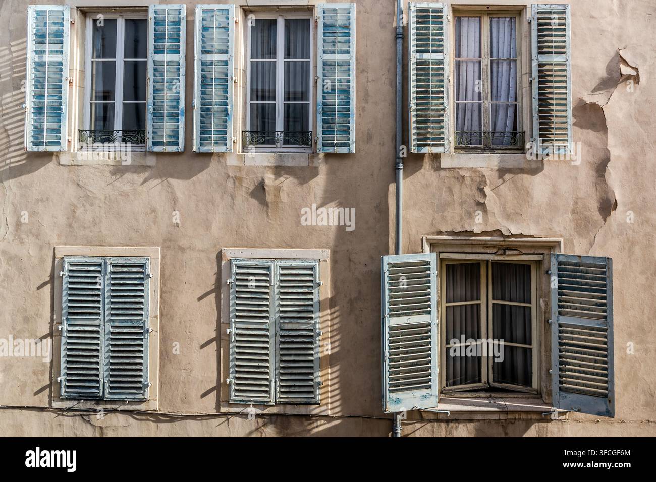 Des volets bleus encadrent plusieurs fenêtres sur une façade de maison usée de la Rue de Guise dans la vieille ville de Nancy, Grand Est, France. L'une des fenêtres est entrouverte, avec un rideau visible derrière elle. Banque D'Images