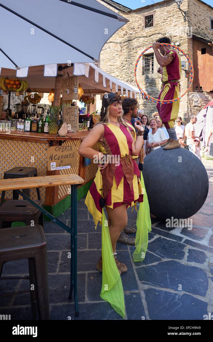 PUEBLA DE SANABRIA, ESPAGNE – 14 AOÛT 2026 : Des artistes de rue en costumes d’époque colorés se tiennent à côté d’un stand de nourriture pendant le marché médiéval annuel Banque D'Images