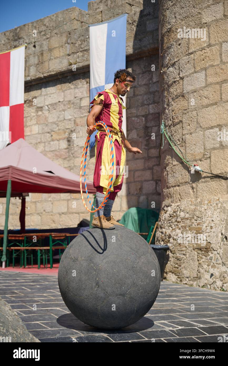 PUEBLA DE SANABRIA, ESPAGNE - 14 AOÛT 2026 : Un artiste portant un costume d'époque coloré équilibre sur un grand ballon tout en tenant des cerceaux de hula-hoop à côté d'une coulisse Banque D'Images
