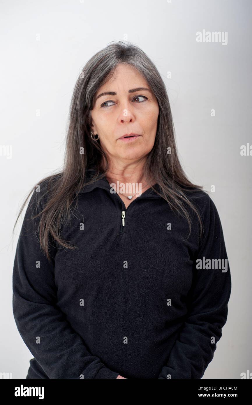 Portrait d'une femme d'âge moyen aux cheveux gris regardant de côté avec une expression pensive. Photo de studio sur fond neutre avec une lumière naturelle douce. Banque D'Images