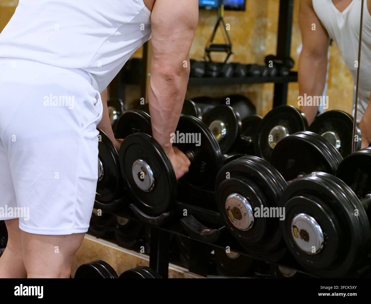 Un plan rapproché en angle latéral d'un homme musclé tendant la main vers un haltère noir lourd sur un support. Son avant-bras bien dessiné et ses veines sont clairement visibles, avec Banque D'Images