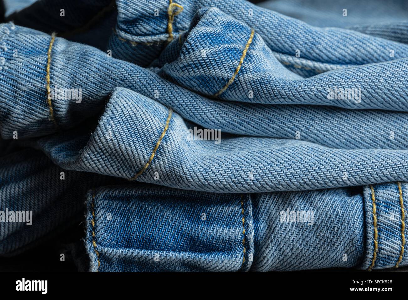 Tissu en jean bleu montrant des détails de texture et des coutures jaunes en fond en gros plan Banque D'Images