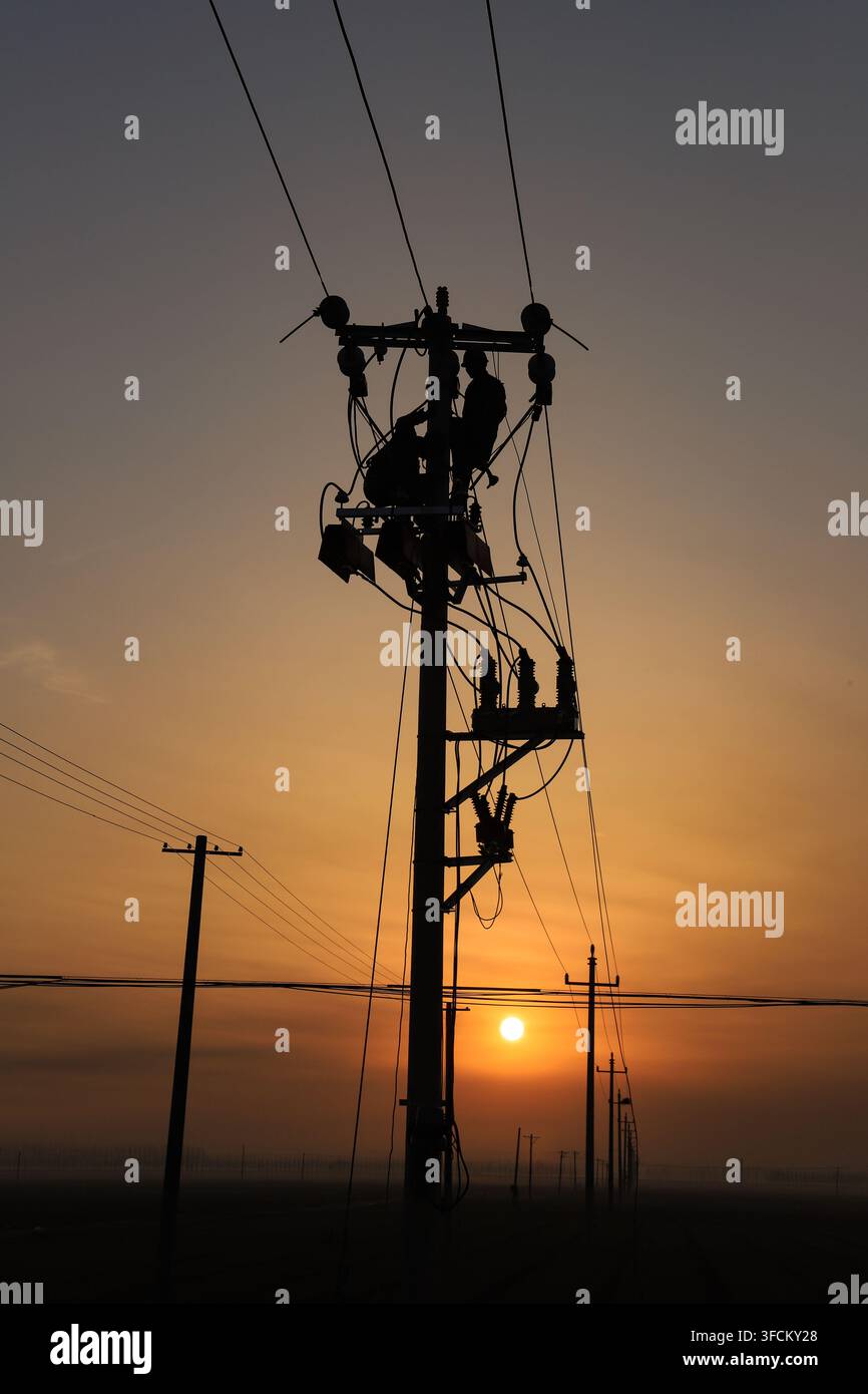 Une silhouette frappante d'un électricien travaillant en hauteur sur un poteau électrique pendant le lever du soleil matinal. Le ciel chaud et coloré avec un orange vif a Banque D'Images