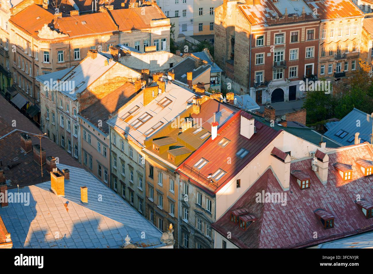 La lumière chaude du soleil projette de longues ombres sur les toits en terre cuite et en métal usés de l'architecture européenne ancienne, mettant en évidence des détails et des textes complexes Banque D'Images