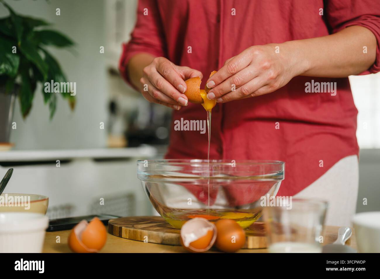 Femme casse un œuf brun dans un bol en verre transparent dans la cuisine Banque D'Images