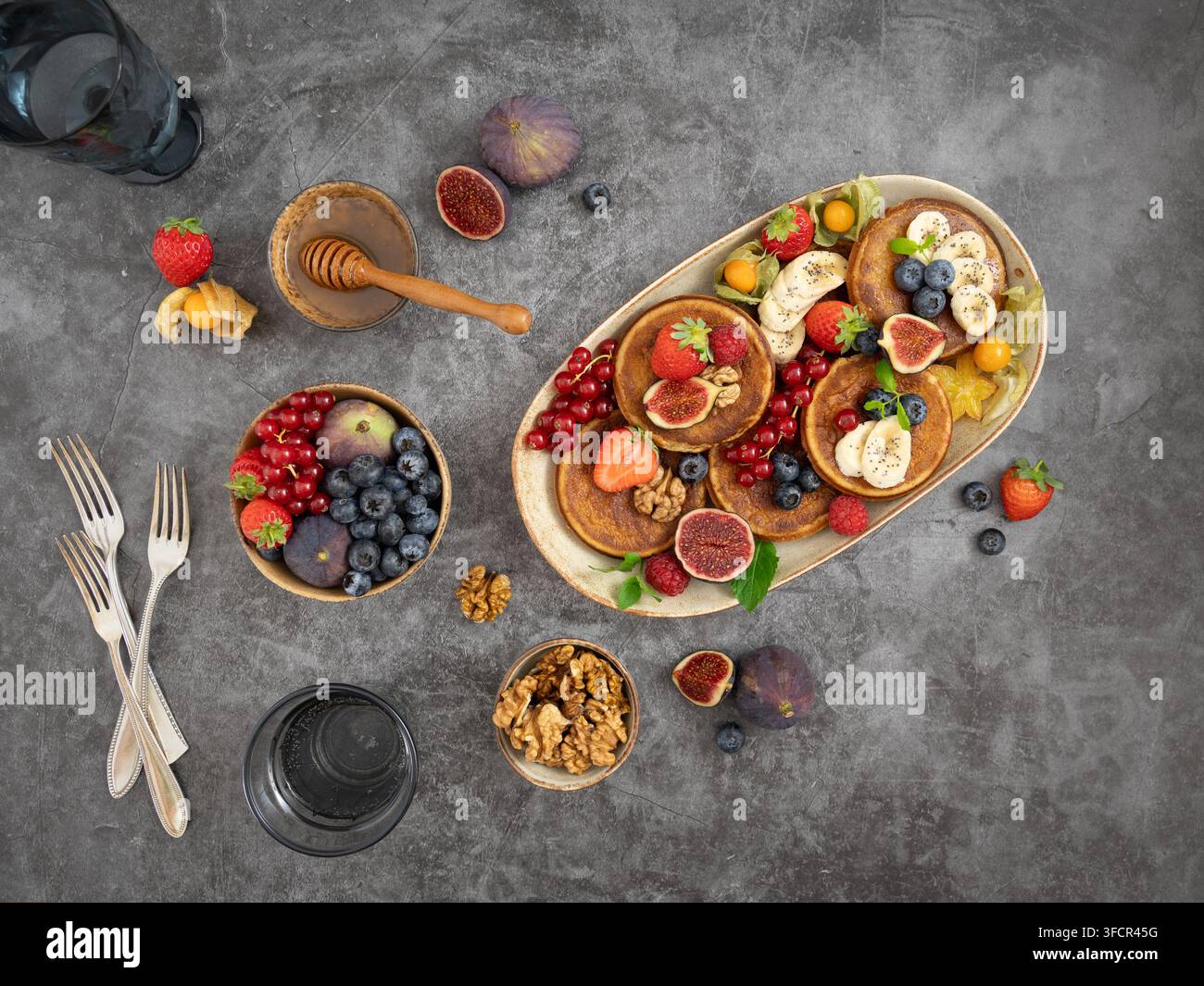 Arrangement de petit-déjeuner en hauteur mettant en vedette des crêpes, des baies, des figues et des garnitures de fruits sur une table rustique Banque D'Images