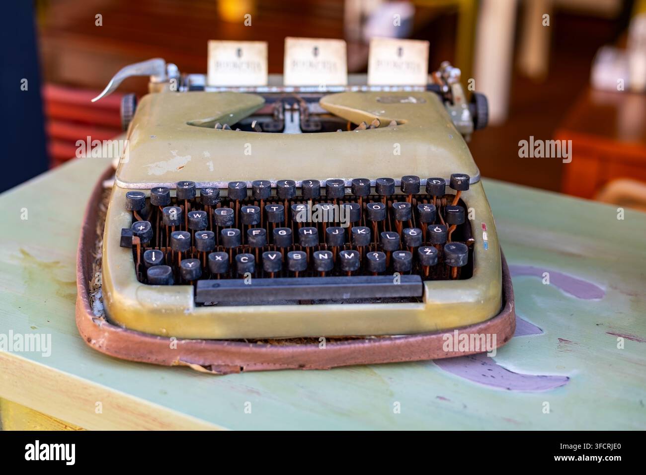Machine à écrire manuelle vintage sur table usée. Machine à écrire manuelle vintage avec des touches noires et un corps olive usé reposant sur une table peinte dans un flou doux Banque D'Images