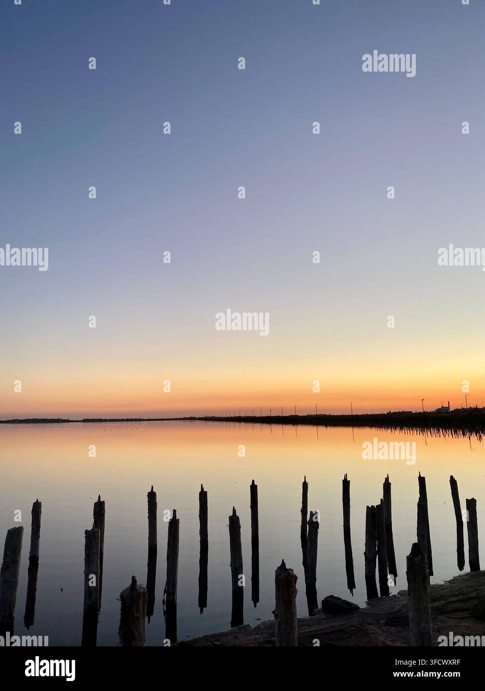 Des poteaux en bois érodés se reflètent dans l'eau immobile sous un doux coucher de soleil orange Banque D'Images