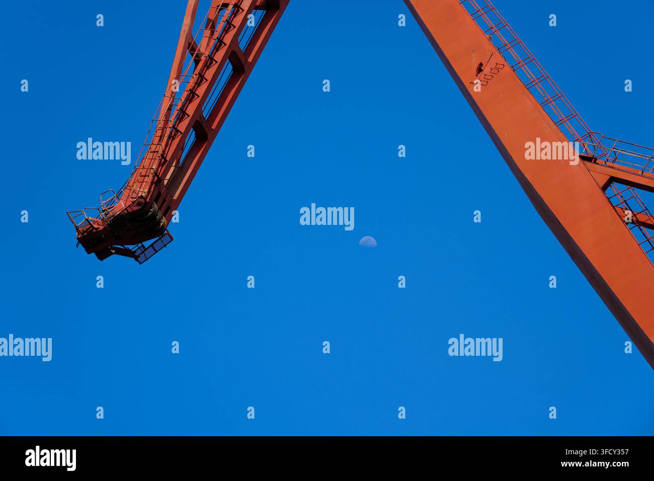 Demi-lune dans un ciel bleu clair encadrée par la structure en acier rouge d'une grue portuaire massive, prise de vue en contre-plongée Banque D'Images