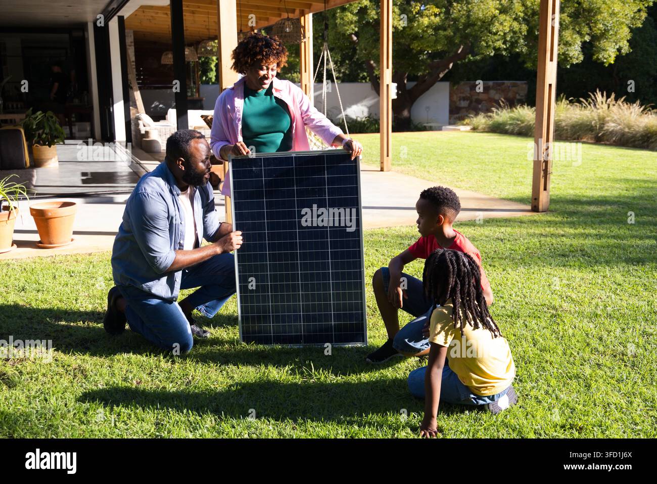 Famille afro-américaine assemblant un panneau solaire sur la pelouse ensoleillée d'une cour arrière près d'une pergola Banque D'Images