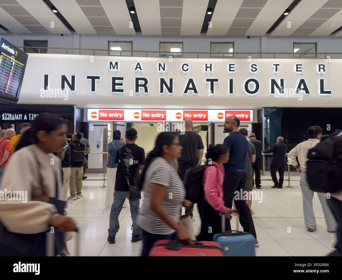 Les voyageurs traversent le hall d'arrivée sous un grand panneau "Manchester International", Angleterre UK Banque D'Images