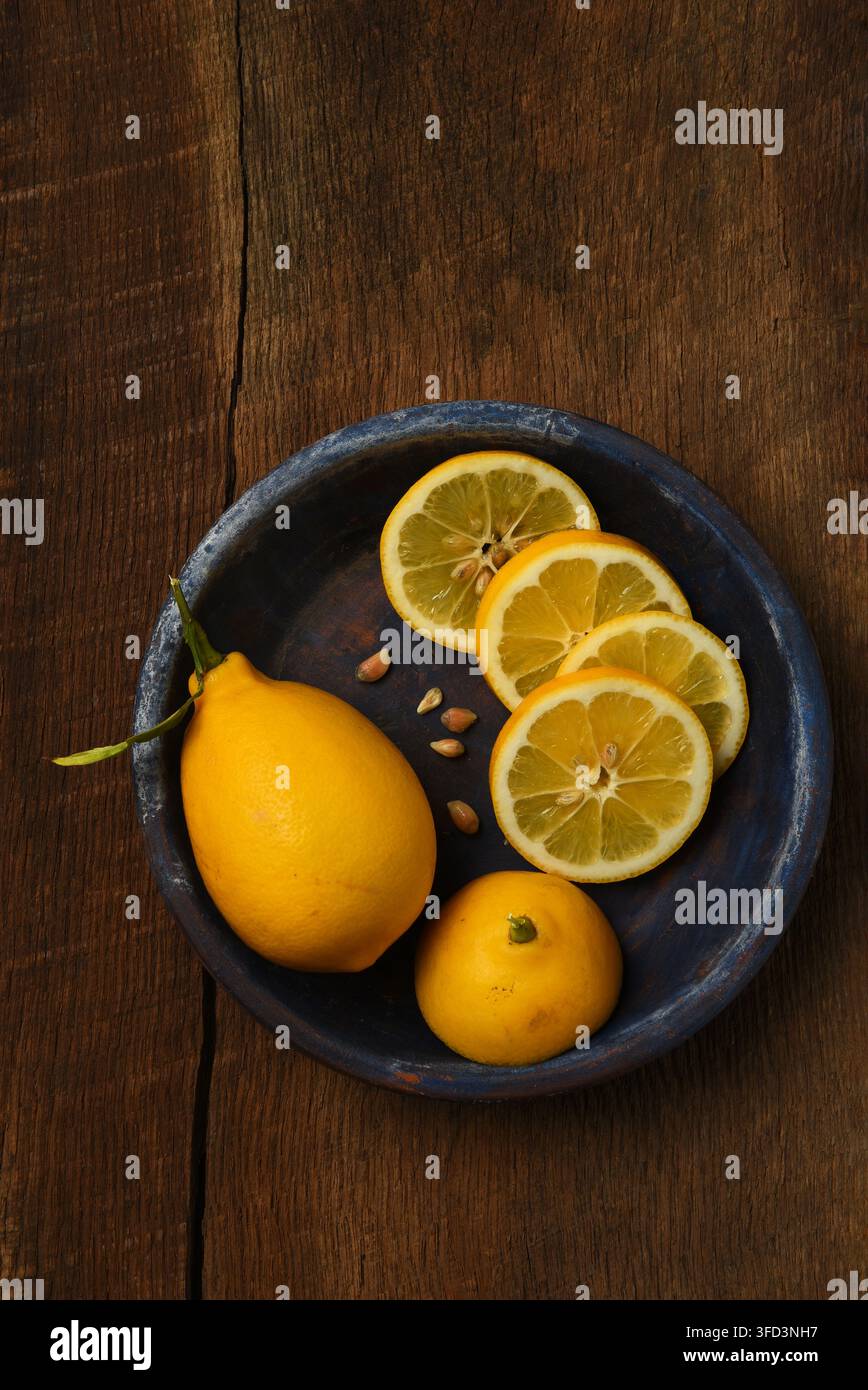 Fflat pond nature morte de citrons. Un citron entier et un citron tranché sur une assiette bleue sur une table en bois rustique. Banque D'Images
