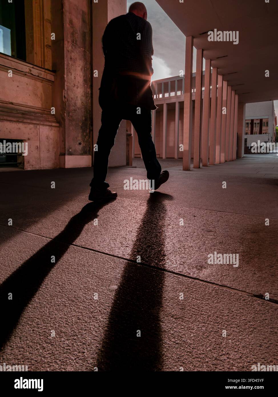 Un passant marche à travers la colonnade de l'île des musées à Berlin-Mitte pendant l'heure dorée, projetant une longue ombre noire. Banque D'Images