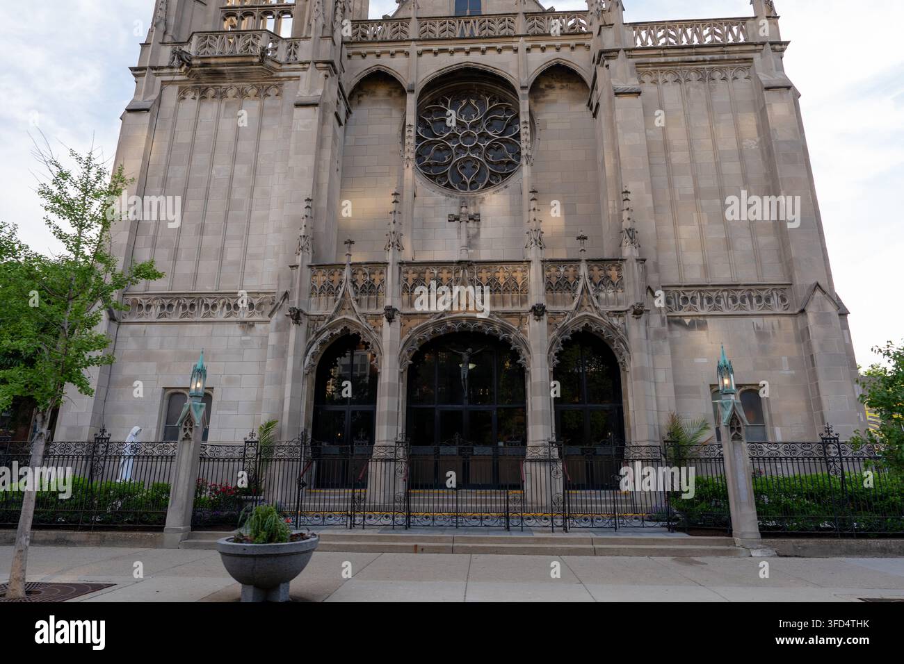 Vue frontale d'une façade d'église néo-gothique historique avec un grand rosace circulaire, des arcs pointus, des ornements en pierre décoratifs et une clôture en fer forgé Banque D'Images