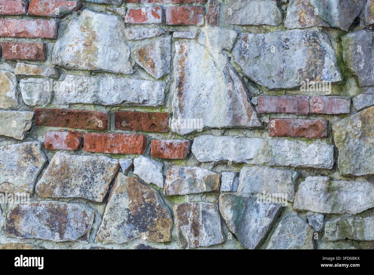 Mur de pierre érodé avec maçonnerie irrégulière et brique rouge apparente Banque D'Images