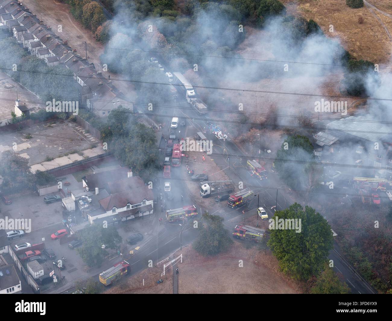 Vue aérienne d'un important incendie près de Carshalton Road, Mitcham, montrant des broussailles brûlées, des bâtiments industriels endommagés et de la fumée, Londres, Royaume-Uni. Banque D'Images