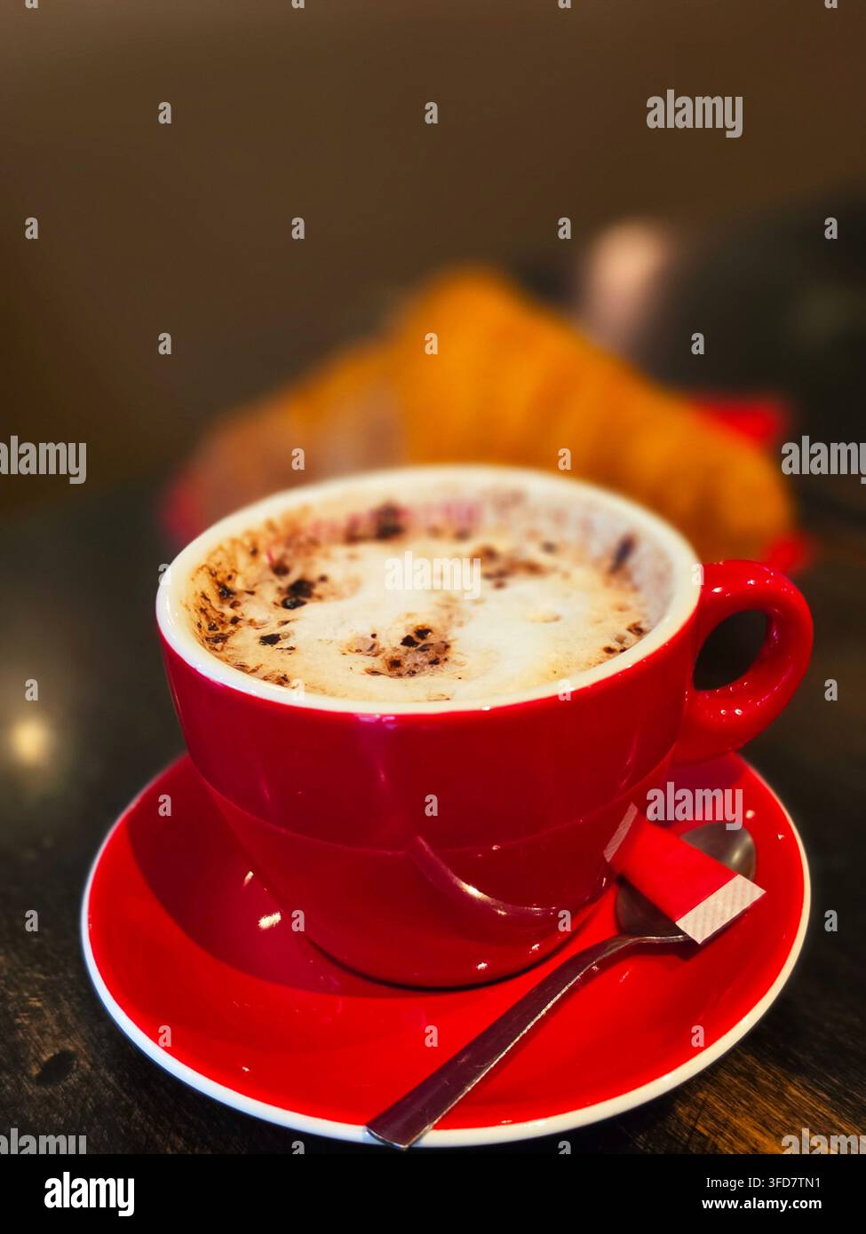 Cappuccino à la mousse épaisse dans une tasse en céramique rouge vif posée sur une soucoupe turquoise. Banque D'Images