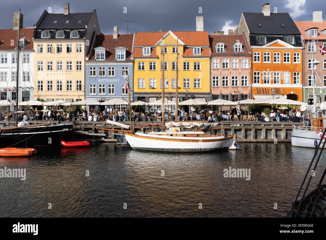 Les visiteurs profitent d'un dîner en plein air le long du canal à Nyhavn, Copenhague, entourés des maisons de ville emblématiques, historiques et colorées du quartier. Banque D'Images