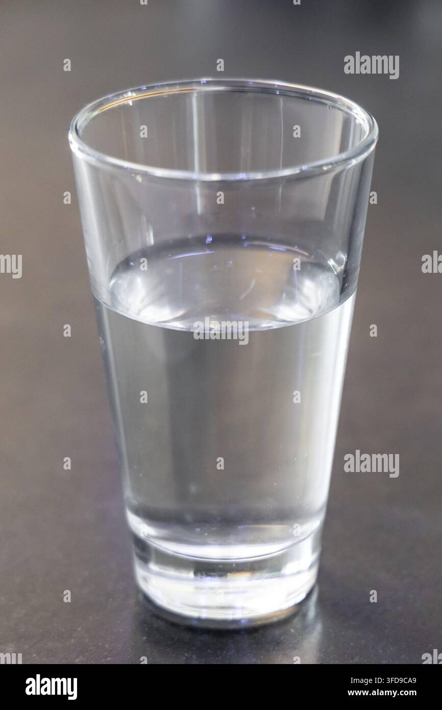 Un simple verre d'eau pure repose sur un plan de travail sombre et légèrement réfléchissant, mettant en valeur sa clarté et sa nature rafraîchissante Banque D'Images