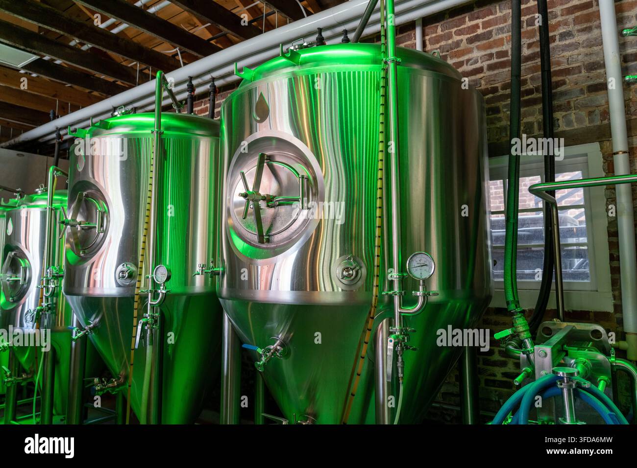 Grands fûts de bière dans une brasserie stockant de la bière en fermentation dans un grand réservoir illuminé par des lumières vertes Banque D'Images