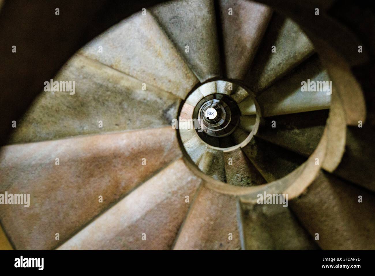 Vue abstraite de dessus d'un escalier en colimaçon en pierre, avec des marches qui s'enroulent étroitement vers un centre circulaire lumineux créant un effet de tunnel hypnotique. Banque D'Images