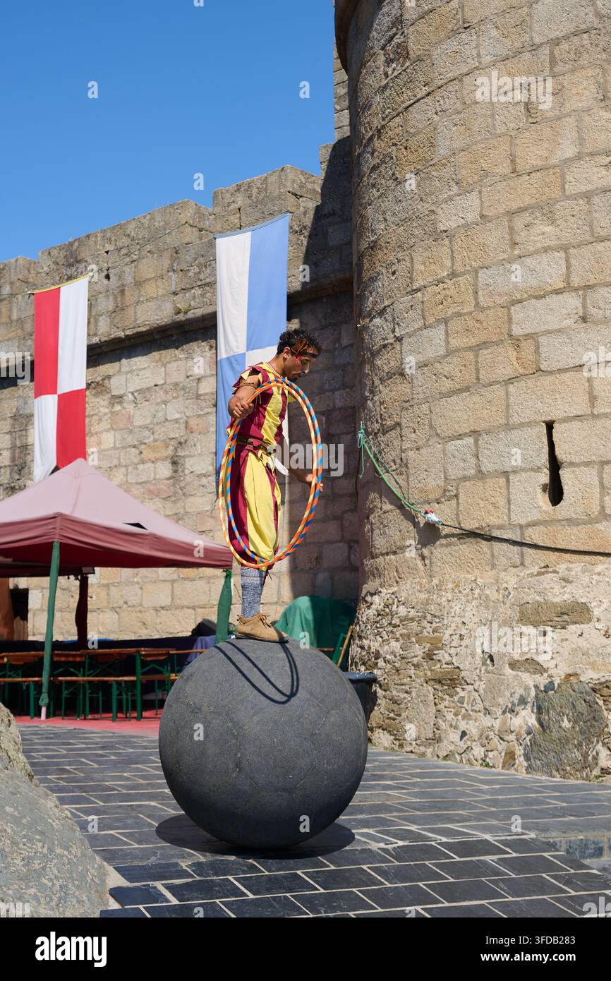 08-14-2026, Puebla de Sanabria, Artiste en costume historique équilibrant sur une grande boule de pierre et tenant des cerceaux de hula hoop, divertissant les visiteurs pendant un Banque D'Images