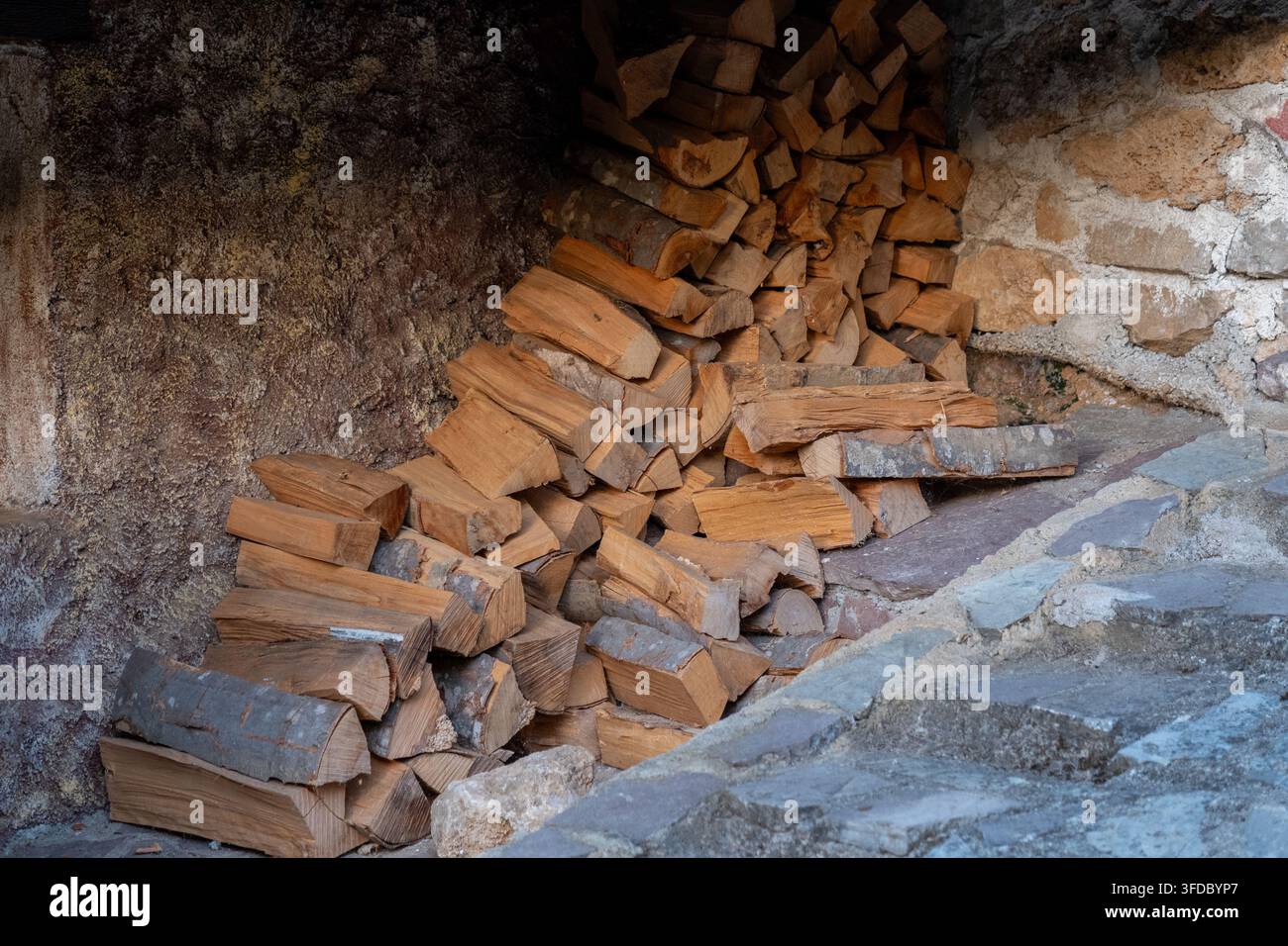Du bois de chauffage empilé remplit une alcôve en pierre rustique à côté d'une surface de maçonnerie rugueuse. Banque D'Images