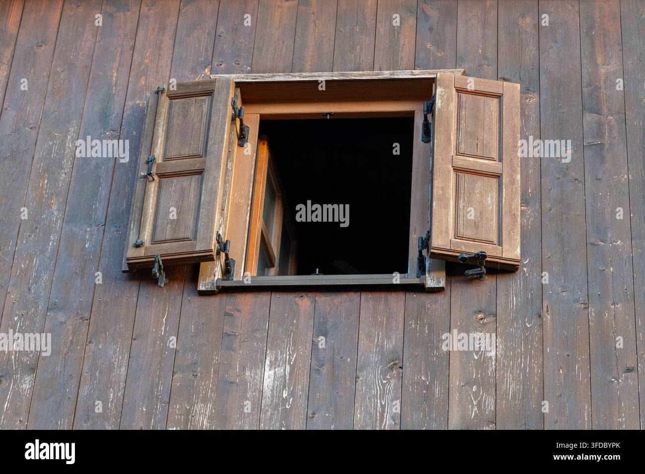 Une fenêtre en bois ouverte avec volets est encastrée dans un mur de planches sombres patinées. Banque D'Images