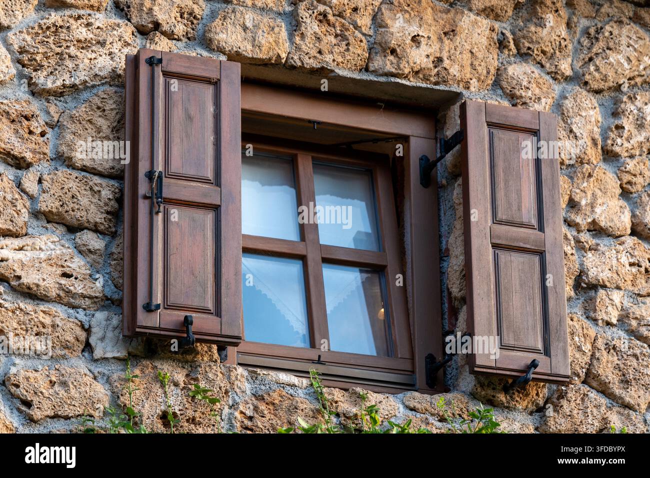 Une fenêtre en bois avec des volets ouverts est encastrée dans un mur de pierre brute sur la façade d'un bâtiment traditionnel. Banque D'Images