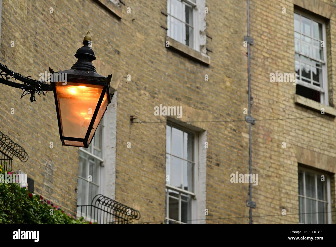 Lampe de rue allumée sur support métallique, vieux bâtiment en briques et fenêtres en arrière-plan Banque D'Images