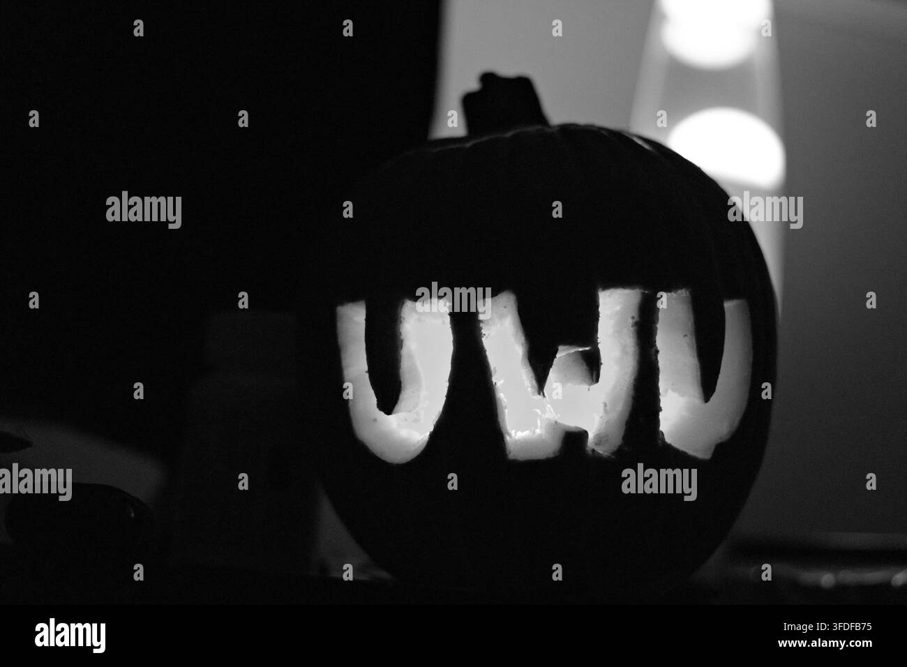Gros plan de lettres sculptées dans une citrouille épelant « UWI », brillant chaleureusement dans l'obscurité. La lumière orange met en valeur les bords rugueux et irréguliers de chaque lettre. Idéal pour H Banque D'Images