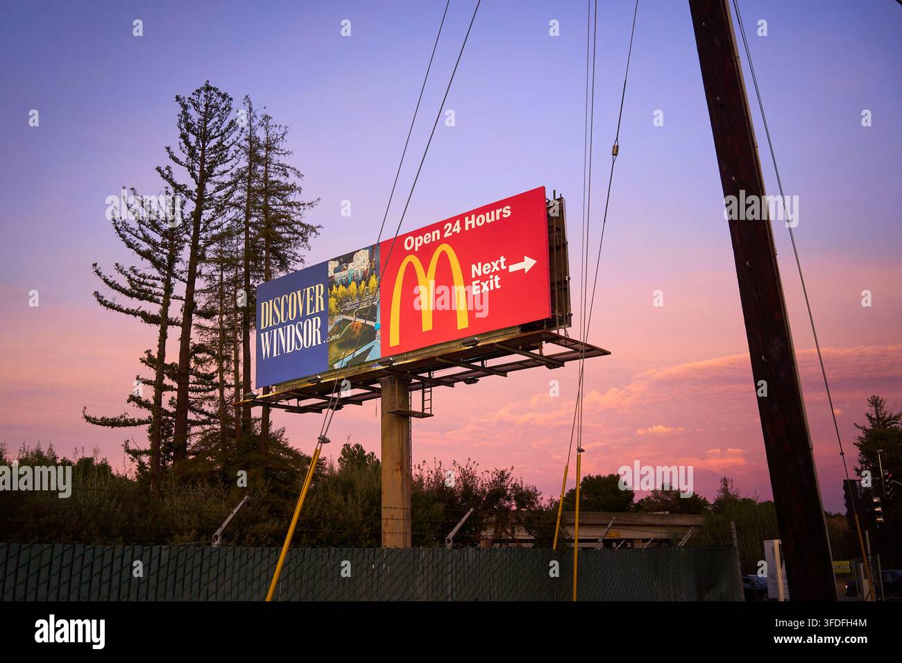 Panneau d'autoroute contre un ciel rose au coucher du soleil faisant la promotion des fast-foods McDonald's et incitant les visiteurs à s'arrêter et à découvrir Windsor. Banque D'Images