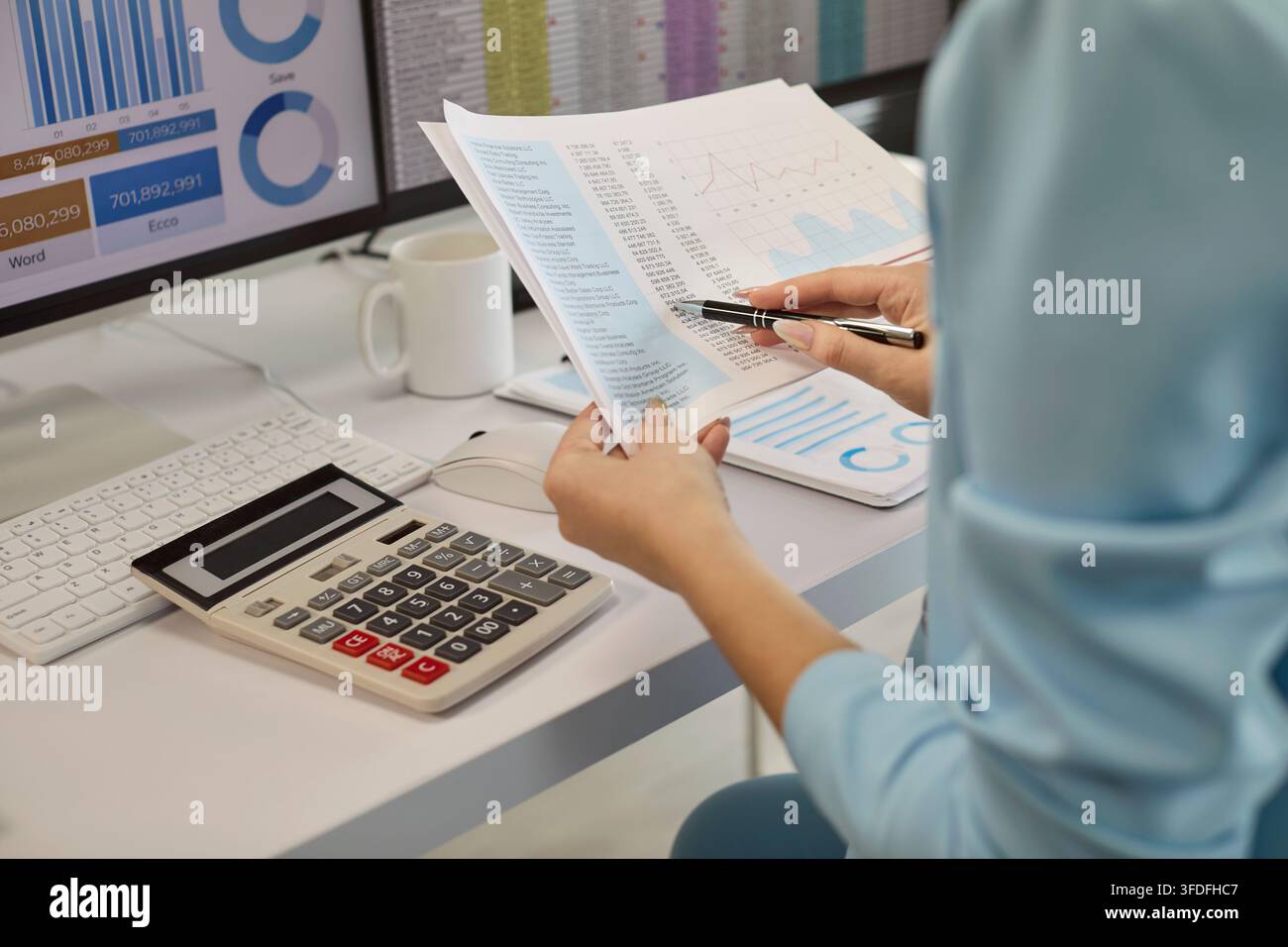 Analyste financière vérifiant des graphiques de données imprimés avec un stylo et une calculatrice Banque D'Images