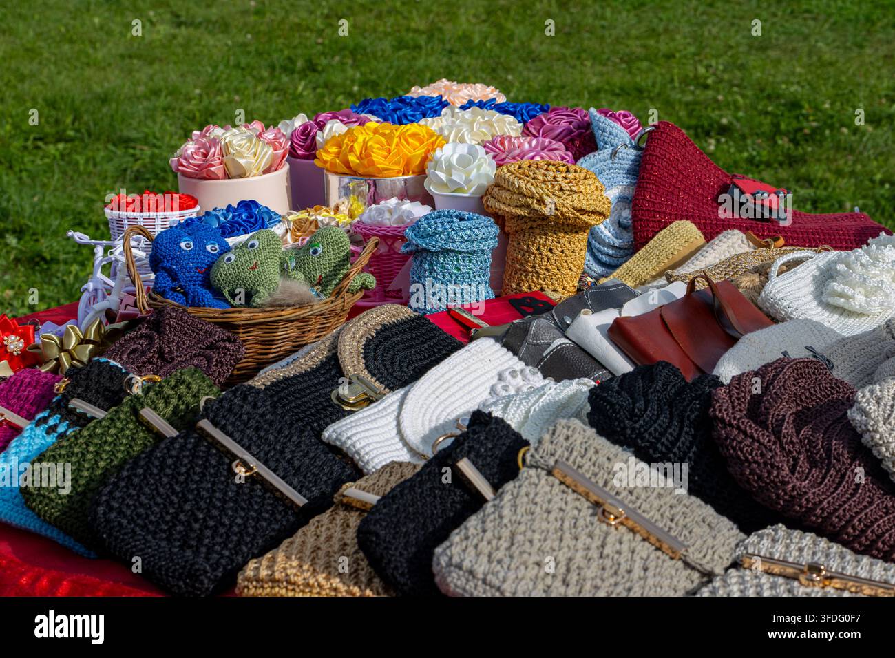 Large sélection d'articles artisanaux exposés sur une table à un marché artisanal en plein air sur un fond de pelouse verte. L'assortiment artisanal comprend du crochet Banque D'Images