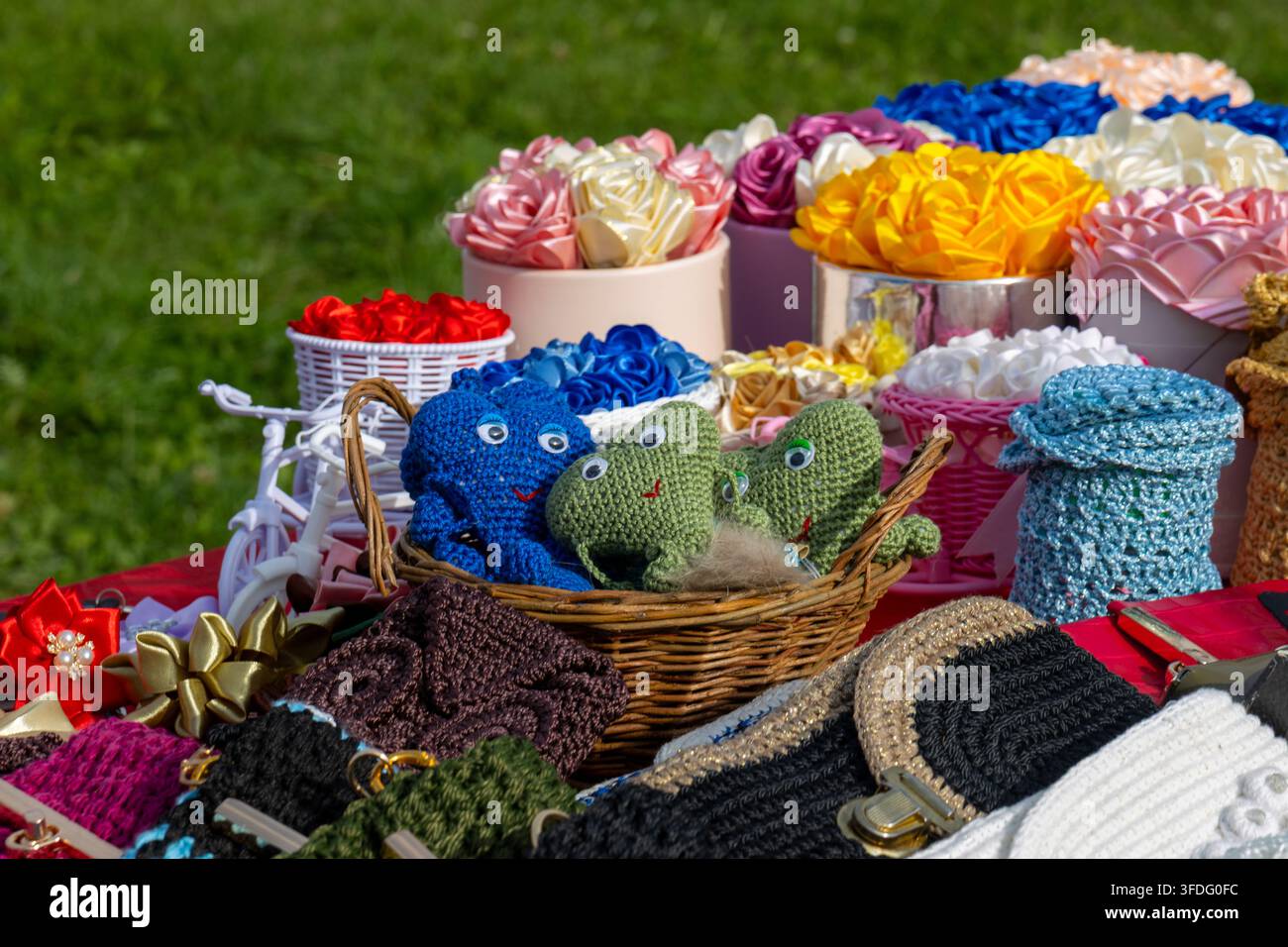 Présentation en gros plan de jouets tricotés artisanaux et d'arrangements floraux artificiels sur une table d'un marché artisanal en plein air. La sélection artisanale comprend le crocodile Banque D'Images
