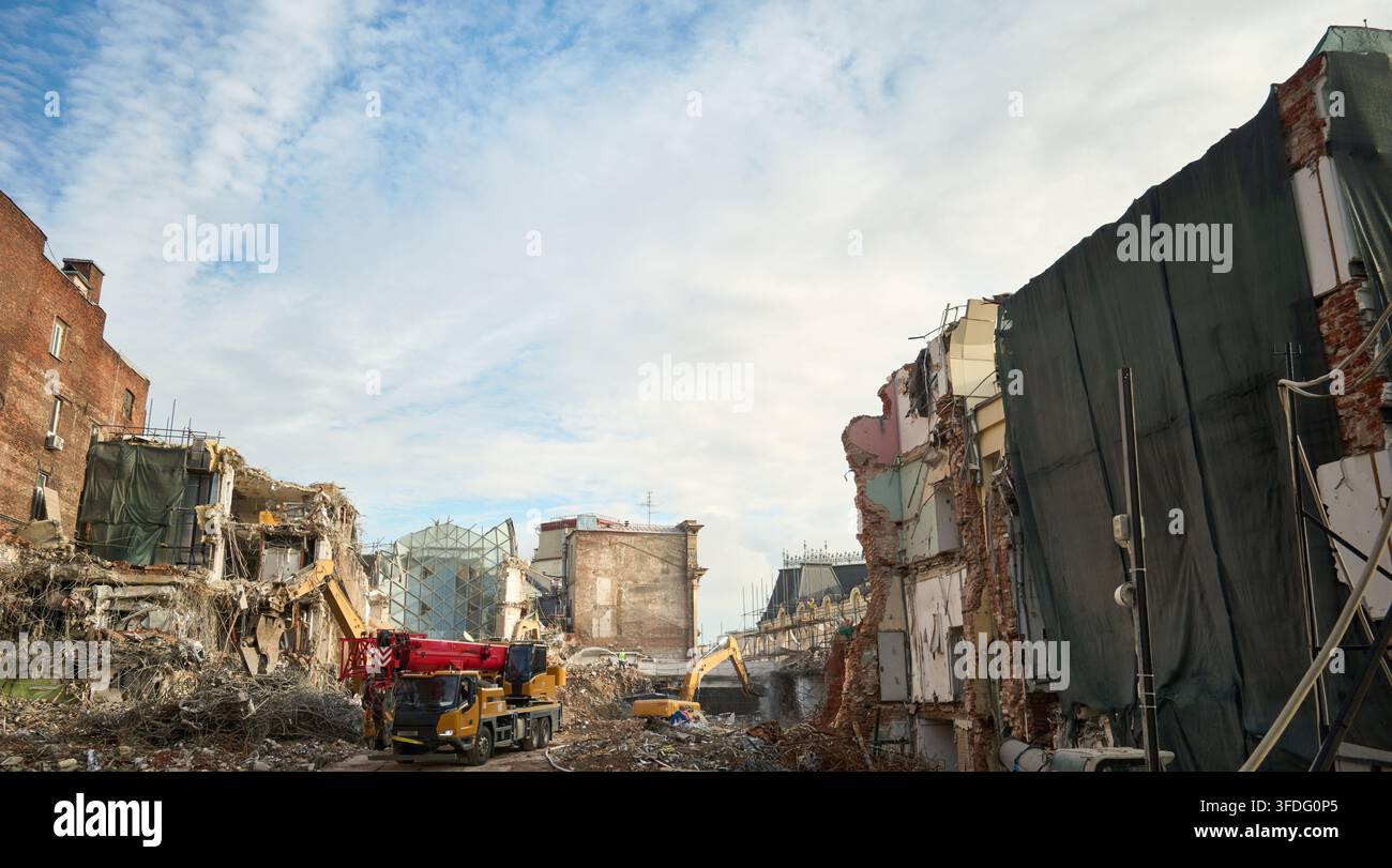 Site de démolition d'un bâtiment urbain avec des engins de chantier sous un ciel nuageux montrant des briques exposées et des gravats, avec démolition, construction, gravats Banque D'Images