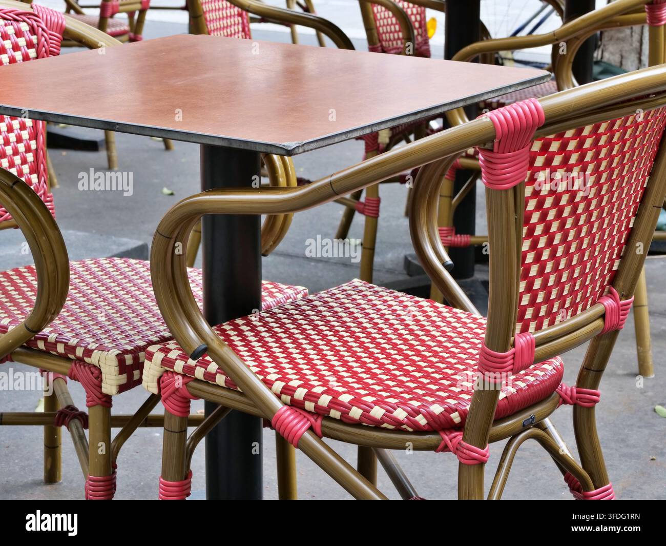 Prise de vue rapprochée détaillée mettant l'accent sur des chaises de bistrot tissées à motif rouge et blanc associées à un plateau de table carré en bois sombre sur une terrasse extérieure de café. C Banque D'Images
