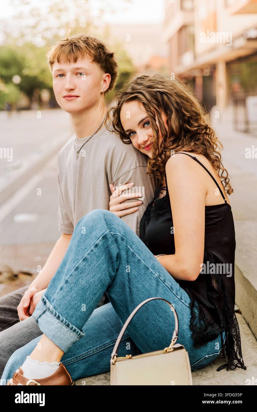 Jeune couple élégant assis ensemble sur un trottoir Banque D'Images
