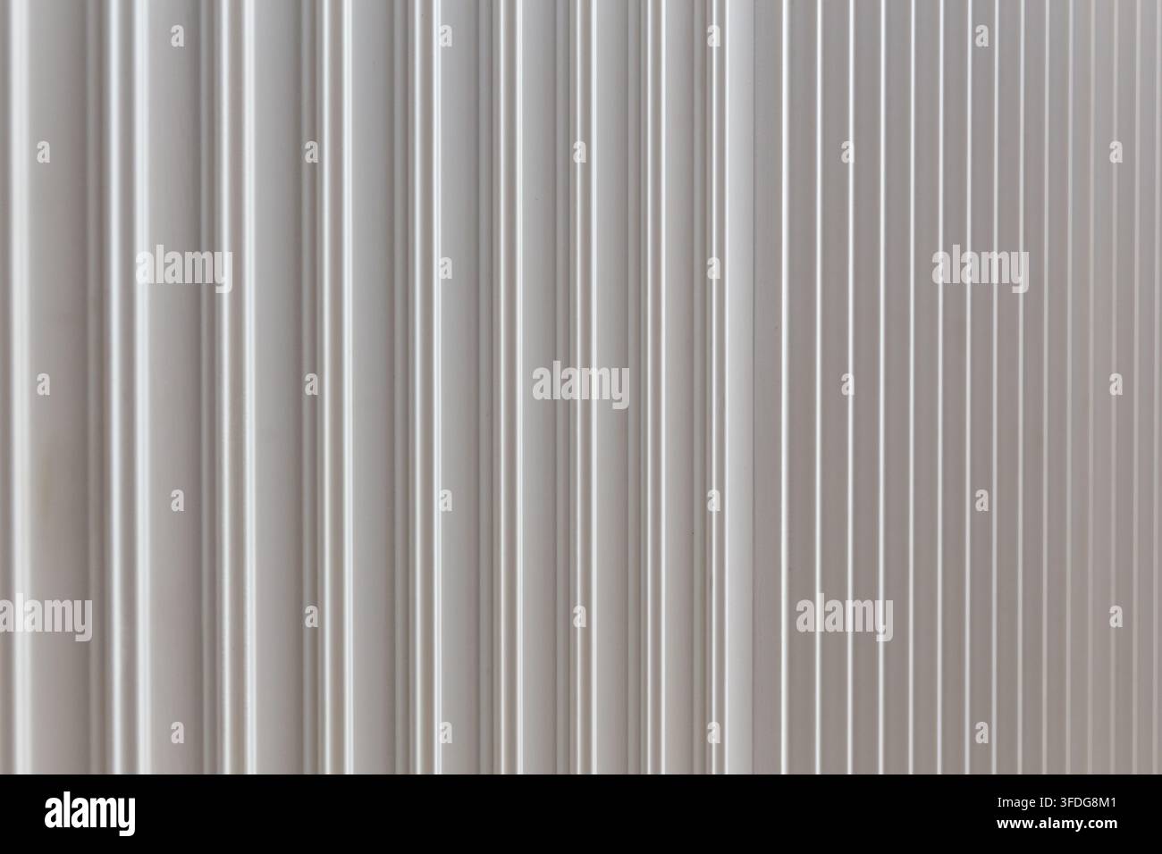 Gros plan d'une texture murale blanche nervurée avec des rainures verticales et une lumière douce, créant un fond architectural abstrait minimaliste épuré. Banque D'Images