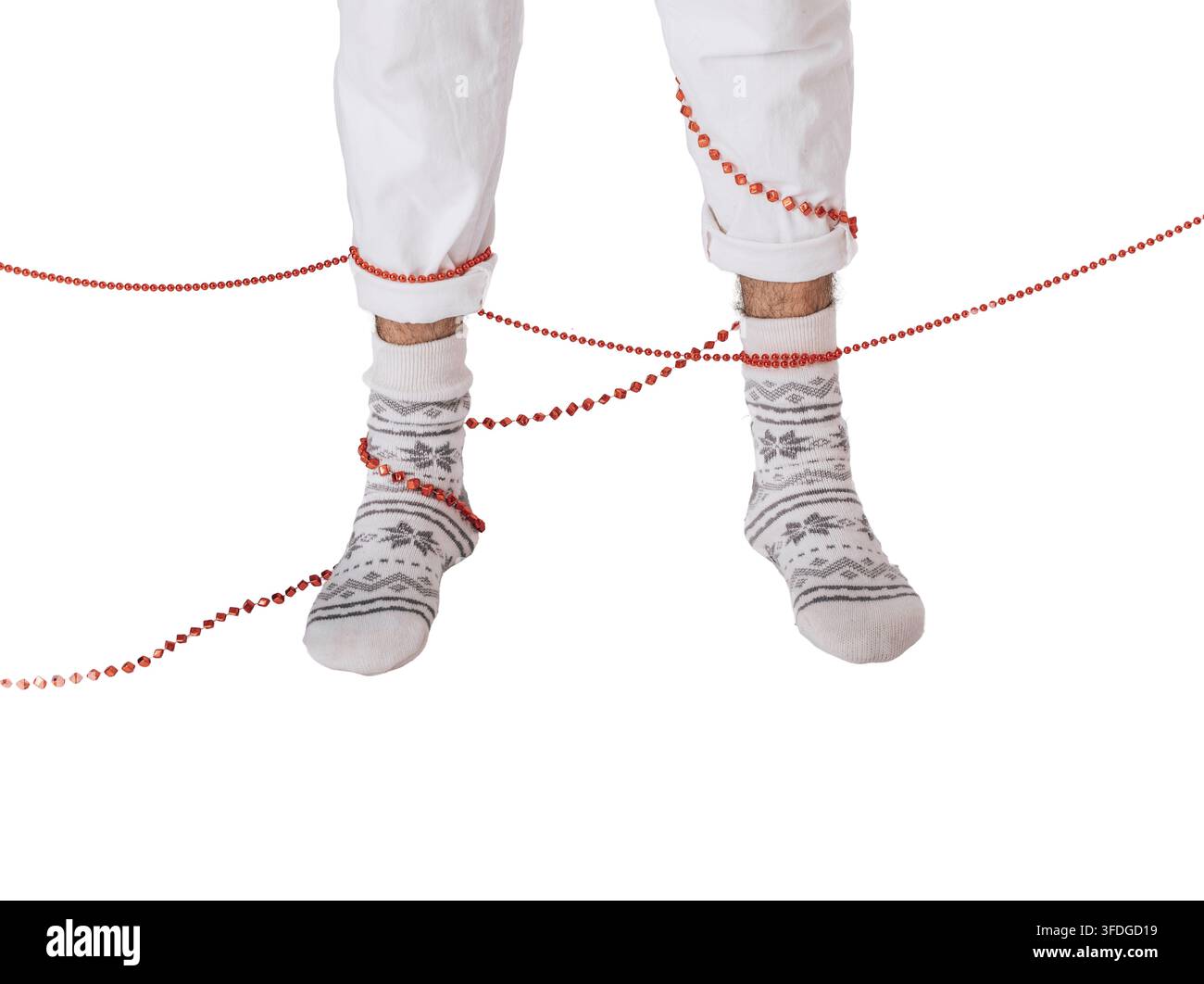 Jambes enchevêtrées dans une guirlande de perles rouges de Noël portant des chaussettes d'hiver douillettes sur un fond blanc isolé, accident de décoration festif des fêtes et rebut saisonnier Banque D'Images