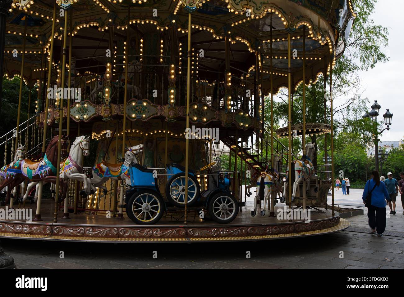 Carrousel illuminé de lumières représentant des chevaux et des calèches ornés dans une zone de parc public. Banque D'Images