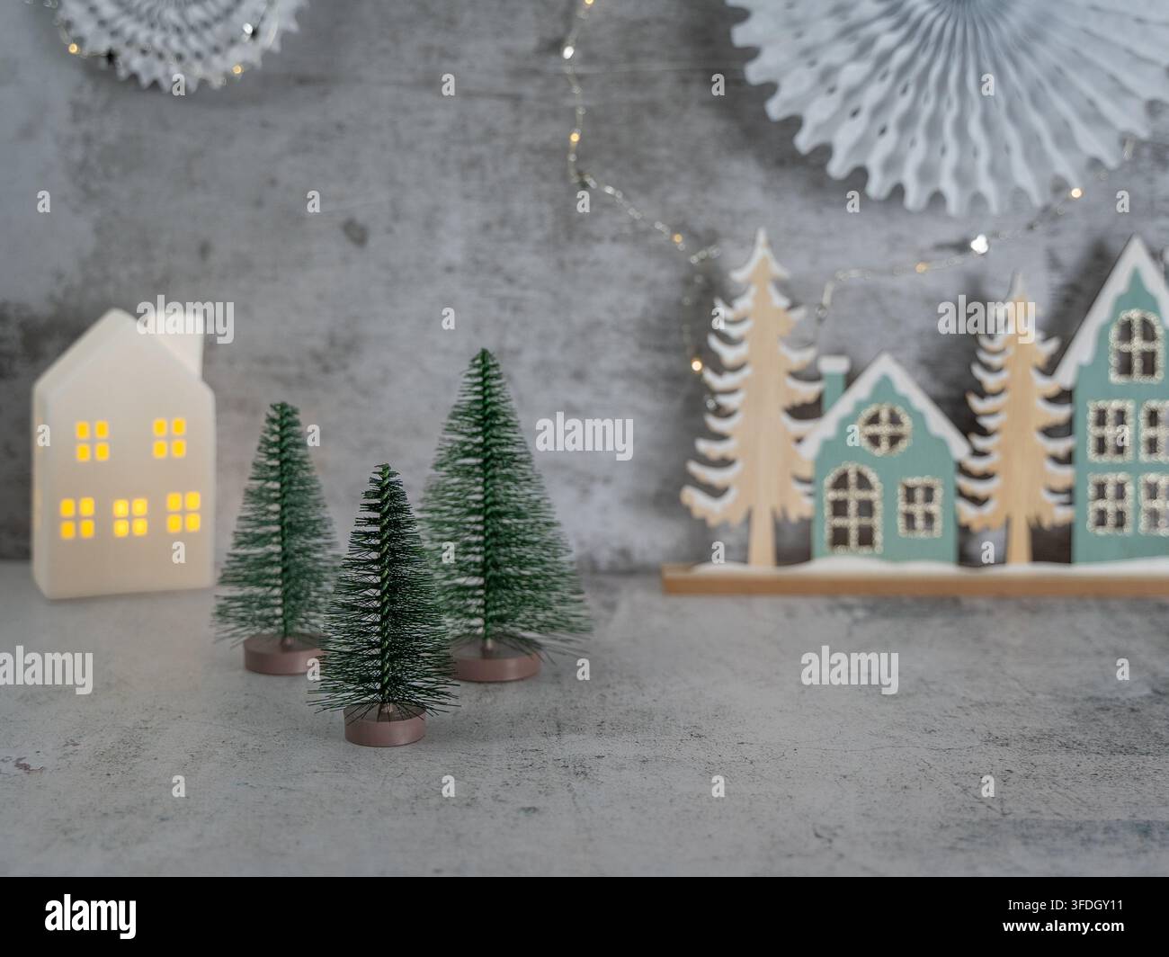 Village de Noël miniature minimaliste avec de petites maisons blanches et des arbres à feuilles persistantes sur un fond d'hiver texturé gris Banque D'Images