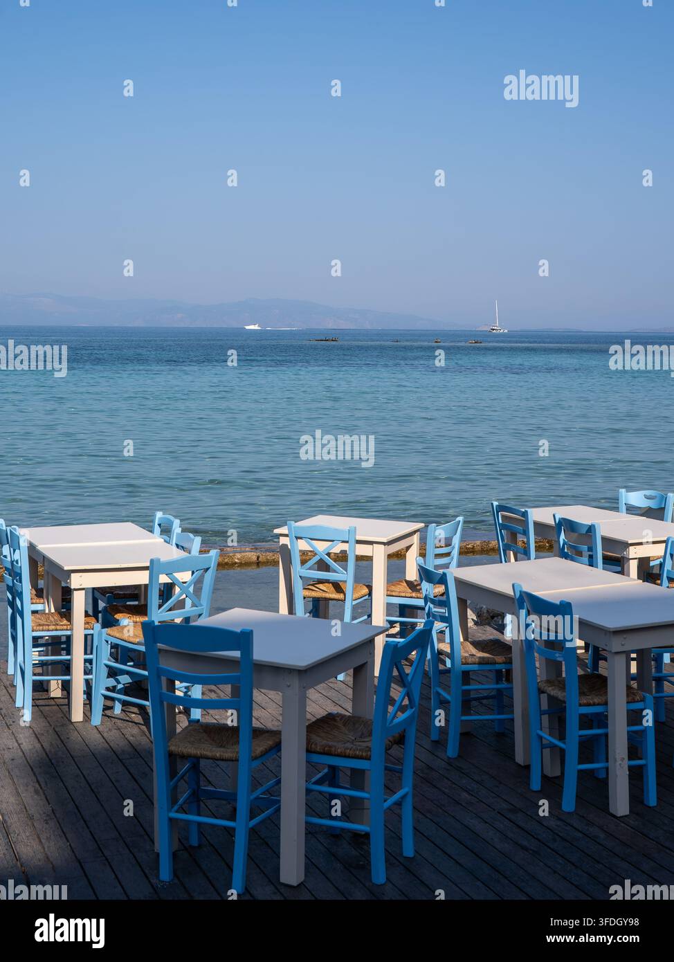 Tables et chaises bleues et blanches sur une terrasse de restaurant en bord de mer avec vue sur la mer Égée calme Banque D'Images