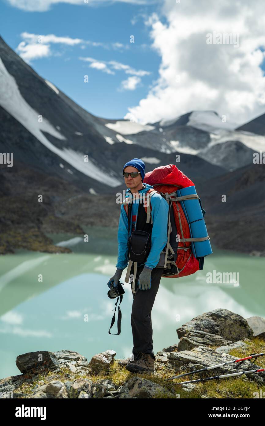 Randonneur avec sac à dos près d'un lac alpin turquoise dans des montagnes enneigées lors d'aventures de trekking en haute altitude Banque D'Images